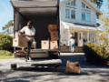 Man unpacking boxes from a moving van in front of a house