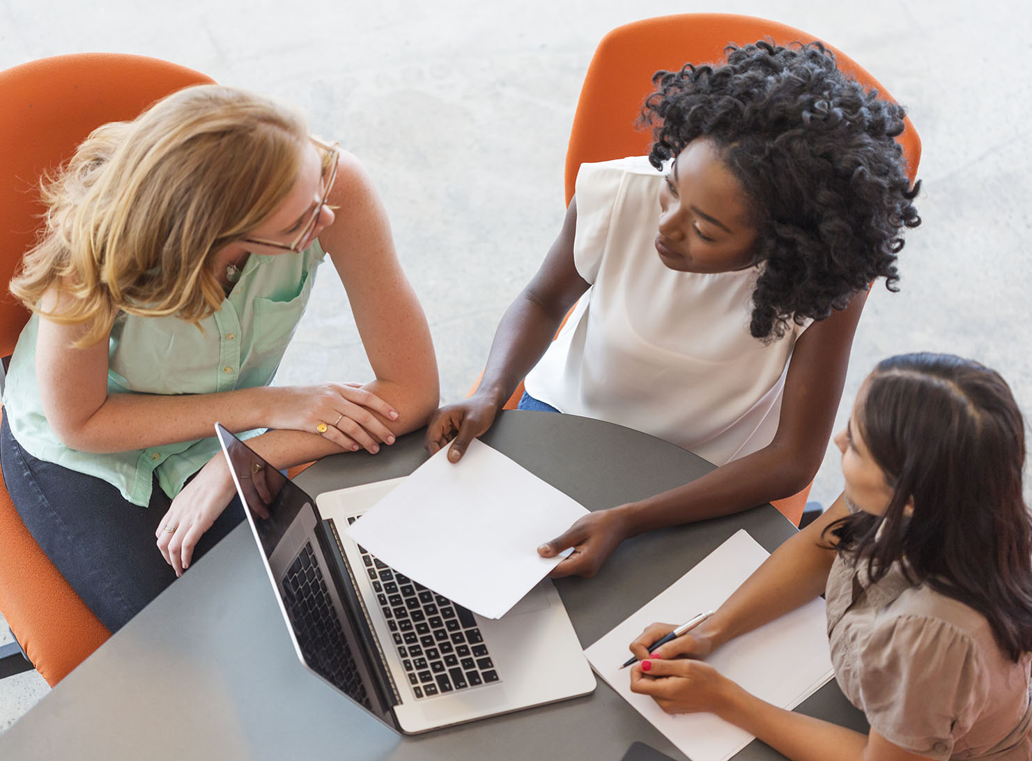 three young diverse businesswomen sitting in casual setting at laptop