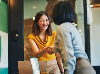 Two businesswomen shaking hands in an office setting.