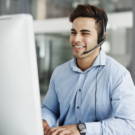 young smiling Caucasian male with headset in front of computer monitor typing